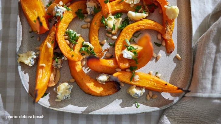 Courge rôtie avec fromage bleu et pignons de pin sur une assiette.