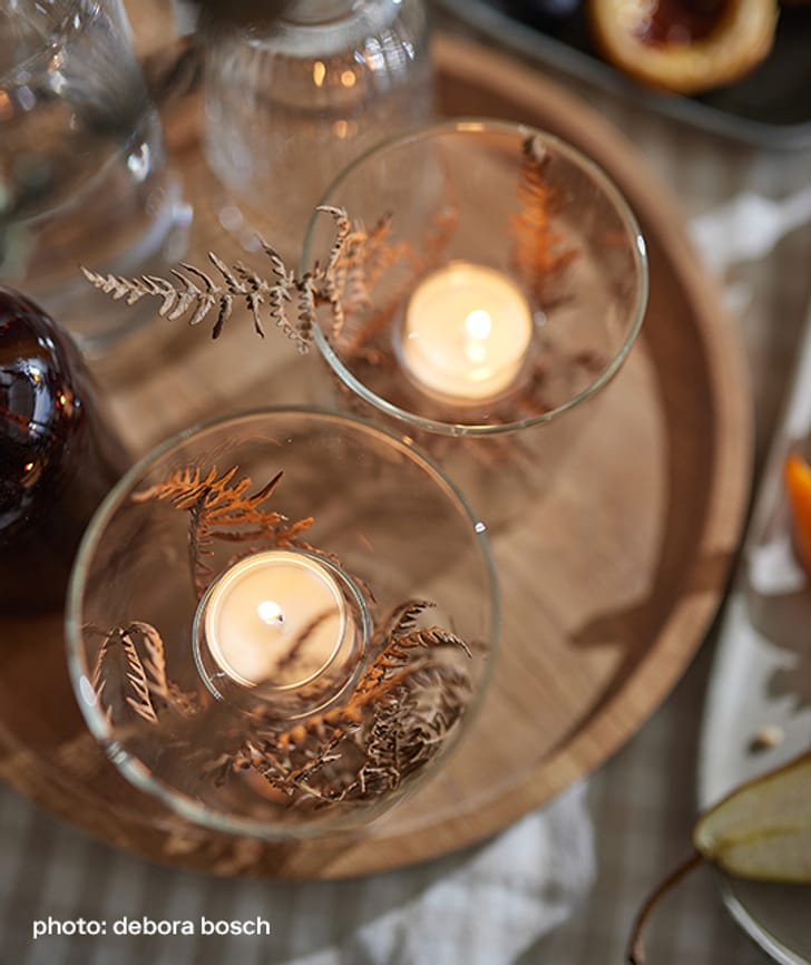 Bougies et fleurs séchées dans des verres sur un plateau.