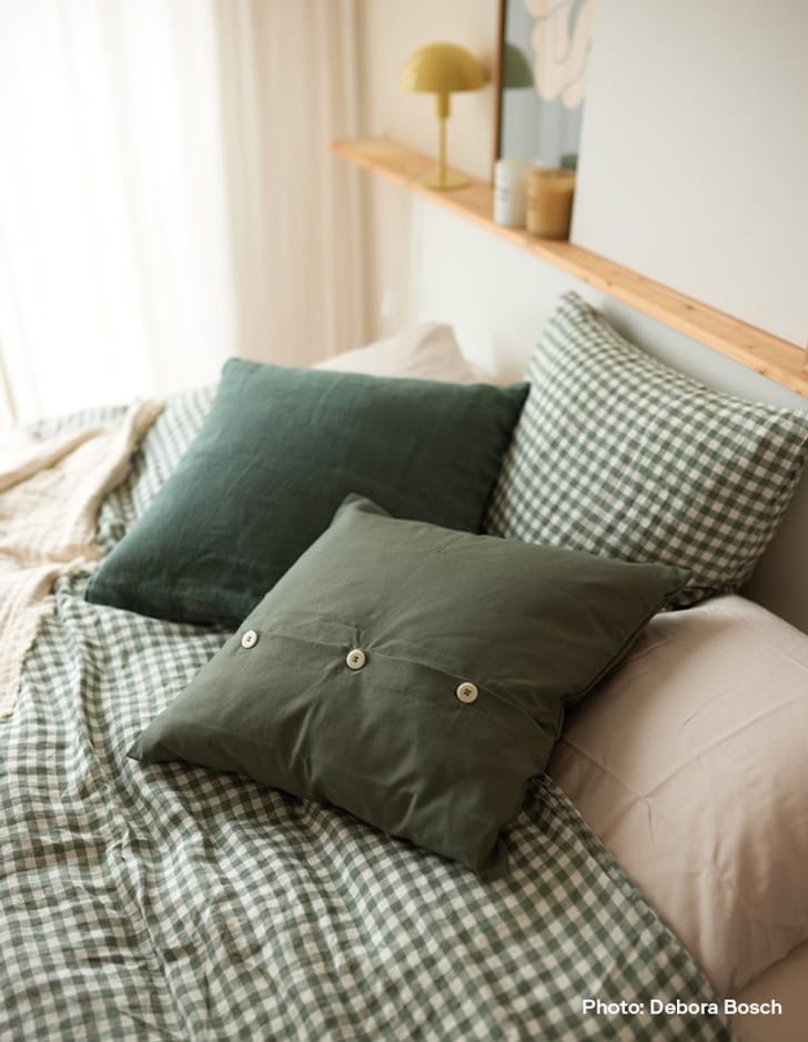 Un lit avec une literie à carreaux verts et des coussins verts, à côté d&apos;une lampe jaune.