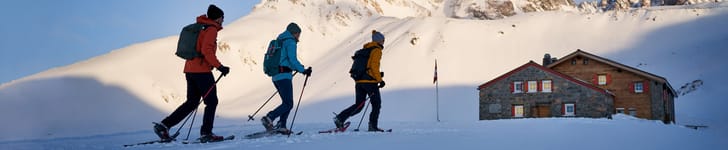 Ein Schneeschuhläufer und zwei Schneeschuhläuferinnen vor einer SAC Hütte.