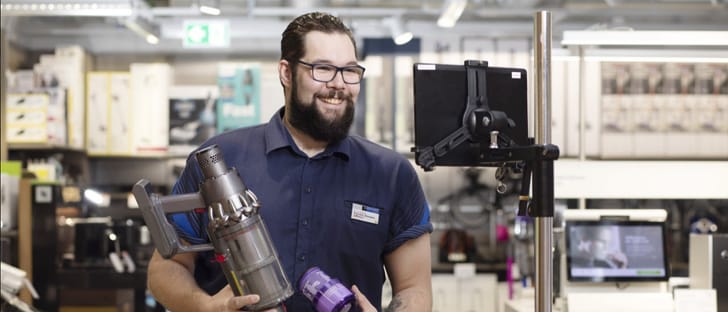 Le consultant vidéo se tient un aspirateur dans la succursale Melectronics et tient un vase dans la caméra pour le client