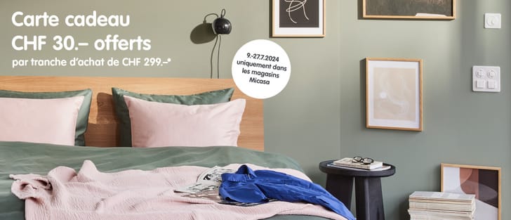 ﻿Scène de chambre à coucher avec un grand lit double, la couleur vert sauge domine et est complétée par des touches isolées de rose (oreiller) ou de bleu roi (couverture)