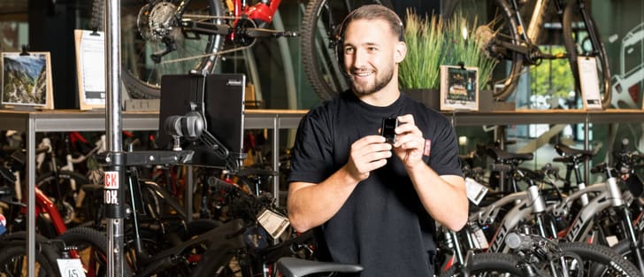 Video-Berater steht in Bikeworld-Filiale und zeigt der Kund:in Fahrräder via Kamera