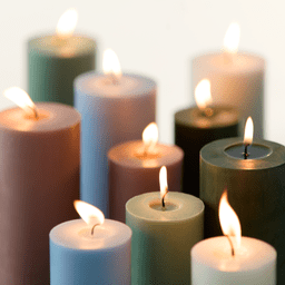 Bougies colorées de différentes tailles allumées sur un fond clair.