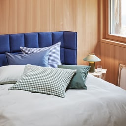Chambre confortable avec lit bleu, fleurs sur la table de chevet et un violon au sol.