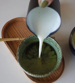 Milch wird in eine Schale mit Matcha-Tee gegossen.