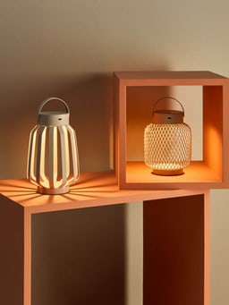 Deux lanternes illuminées aux couleurs chaudes sur une étagère orange.