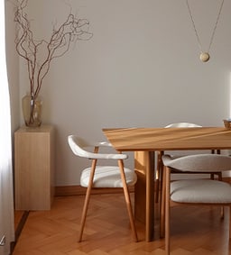 Un coin repas élégant avec une table en bois et des chaises rembourrées, décoré avec un arrangement de branches raffiné.