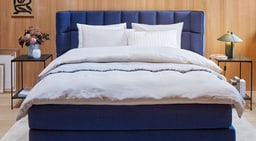 Vue frontale d&apos;une chambre avec lit bleu, literie blanche et tables de chevet de chaque côté.