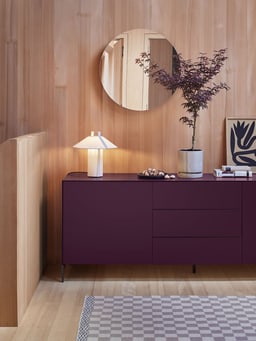 Stilvolles Wohnzimmer mit lila Sideboard, runder Spiegel und dekorative Lampe.