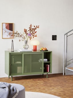 Modernes Wohnzimmer mit grünem Sideboard und Tischlampe auf einem Bücherstapel.
