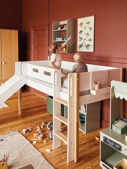 Chambre d&apos;enfant avec un lit mezzanine, un toboggan intégré, des jouets au sol et deux enfants regardant une affiche de dinosaures au mur.