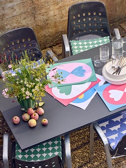 Table de jardin avec sets de table colorés, fleurs et pommes.