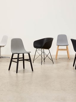 Verschiedene moderne Stühle in Grau und Schwarz auf einem hellen Boden.