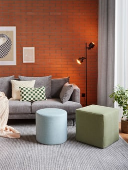 Gemütliches Wohnzimmer mit grauem Sofa, bunten Kissen und moderner Stehleuchte.