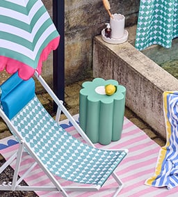 Une chaise longue avec motif géométrique à côté d&apos;une petite table avec un citron, entourée de textiles rayés et à motifs.