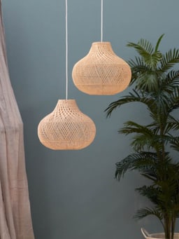 Deux lampes suspendues en matériau naturel tressé devant un mur bleu, à côté d’une plante d’intérieur.