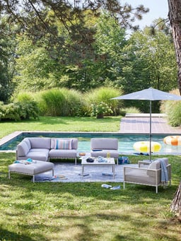 Scène de jardin relaxante avec meubles lounge et parasol près de la piscine.