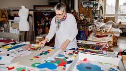 Person arbeitet in einem kreativen Atelier mit bunten Stoffen und Designs.