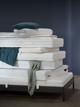 Pile de matelas avec un coussin bleu et une couverture.