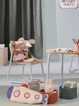 Chambre d’enfant avec jouets, peluches sur une chaise et table avec matériel de dessin.