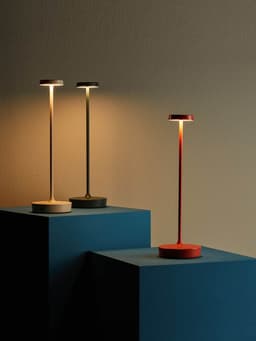 Trois lampes de table fines en blanc, noir et rouge sur des socles bleus.