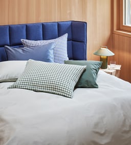 Gros plan d&apos;un lit avec une tête de lit bleue et plusieurs coussins dans des tons de bleu et à carreaux.