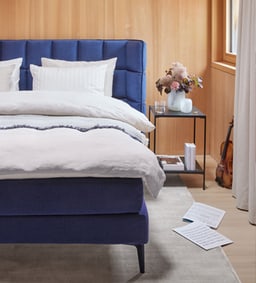 Chambre avec lit bleu, literie blanche et une table de chevet avec des fleurs et un violon à côté.