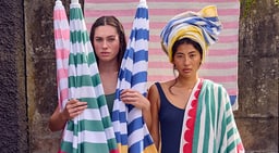 Deux personnes en maillot de bain tiennent des parasols et serviettes rayés.
