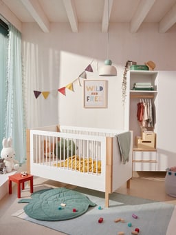 Helles Kinderzimmer mit Krippe, Spielzeugen und hängender Lampe.