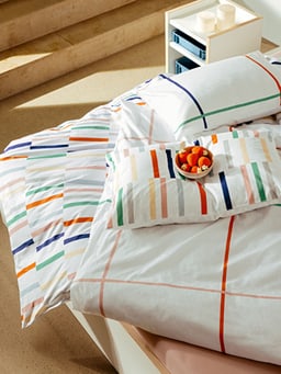 Lit avec draps rayés multicolores et une assiette de fruits.