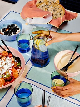 Table avec des assiettes colorées, une salade, du pain et une carafe d&apos;eau avec des baies.