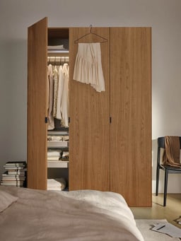 Armadio moderno in legno con anta aperta e abiti chiari.