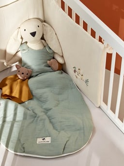 Lapin en tissu dans un sac de couchage avec peluche et couverture dans un lit de bébé.